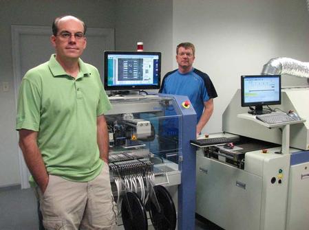 Applied Control & Measurement, LLC, is a former PCB design start-up that now does volume assembly of the very boards it generates. Shown is Brian L. Gery, Owner and Founder (left), and Michael Weil, Director of Operations. They are alongside some of the Manncorp equipment that will achieve targeted production goals -- including the highly flexible MC series pick and place machine and the CR-4000C lead-free reflow oven with KIC Auto Focus Power software. 